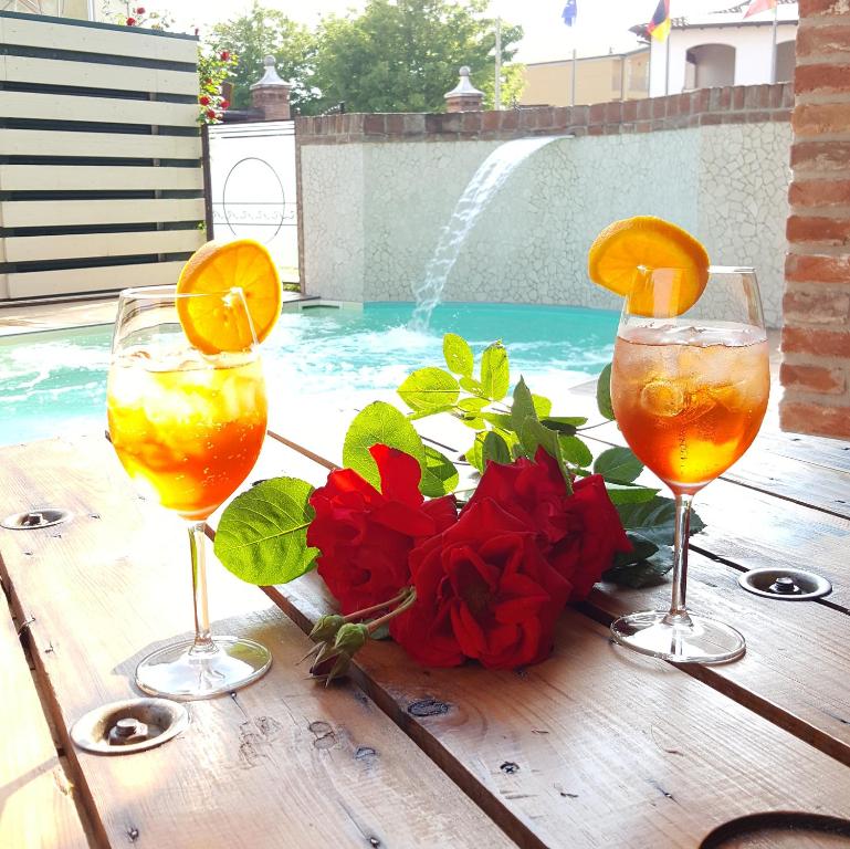 3 copas de vino sentadas en una mesa de madera junto a una piscina en Luna Residence Hotel, en Casalmaggiore