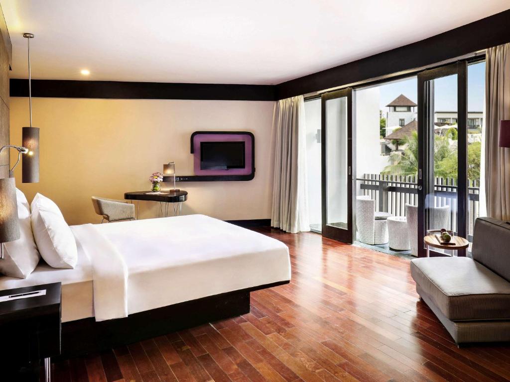 a bedroom with a large white bed and a tv at Pullman Bali Legian Beach in Legian