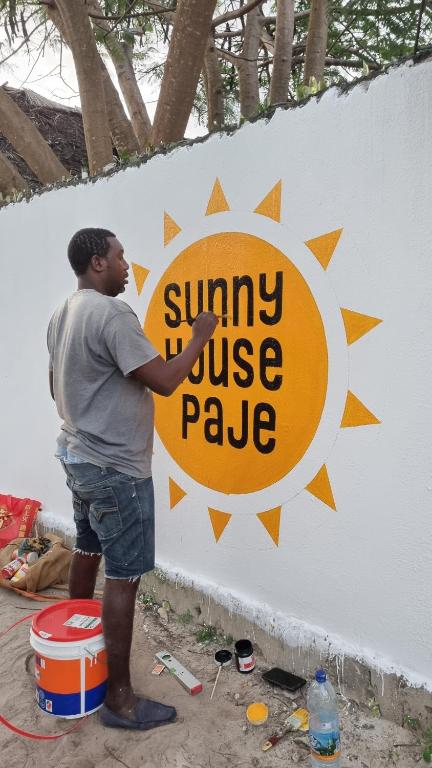 帕傑的住宿－Sunny House Paje，站在墙上标志旁的人