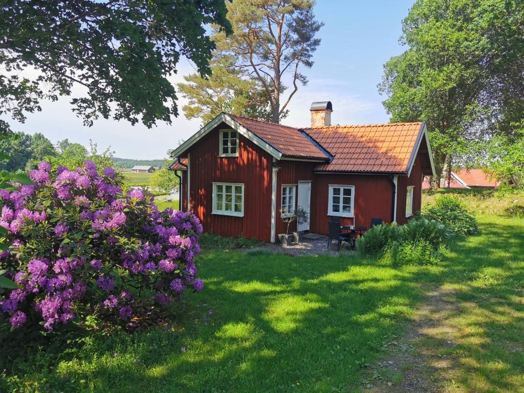 una casa roja en un patio con flores púrpuras en Torpet, en Sollebrunn