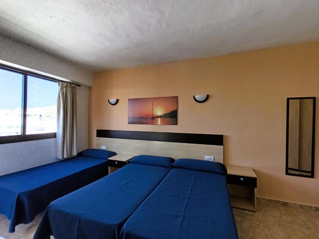 a bedroom with two blue beds and a window at Hostal Horizonte in San Antonio