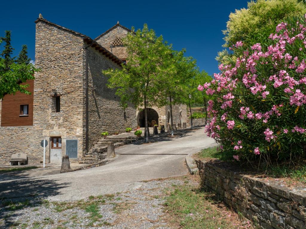 a road in front of a stone building with pink flowers at Casa Cambra in Aínsa