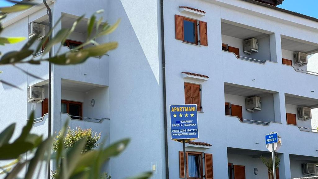 a white building with a blue sign in front of it at Apartments Kvarner in Malinska