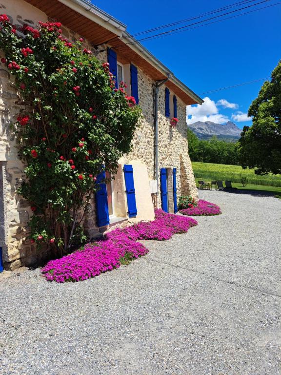 a building with blue doors and pink flowers in front of it at APPARTEMENT BEAU SOLEIL in La Bâtie-Neuve