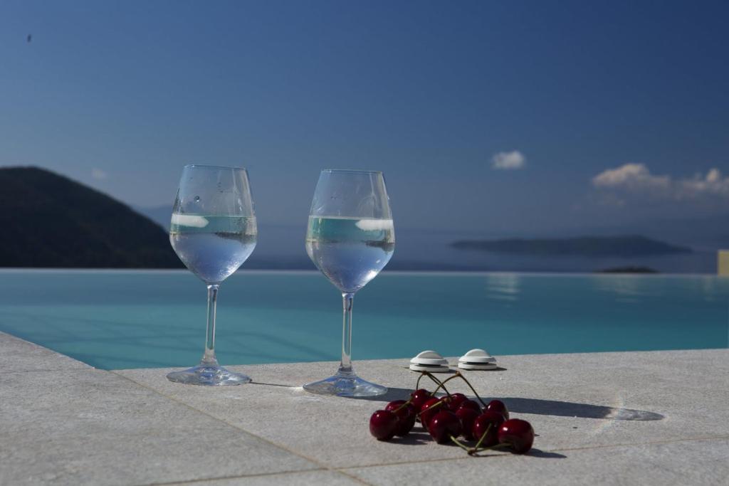 two wine glasses and some cherries next to a pool at Ilios villa in Fternón