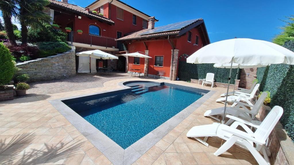 a swimming pool with two white chairs and an umbrella at VILLA LAURA Rooms & Pool in Fossano