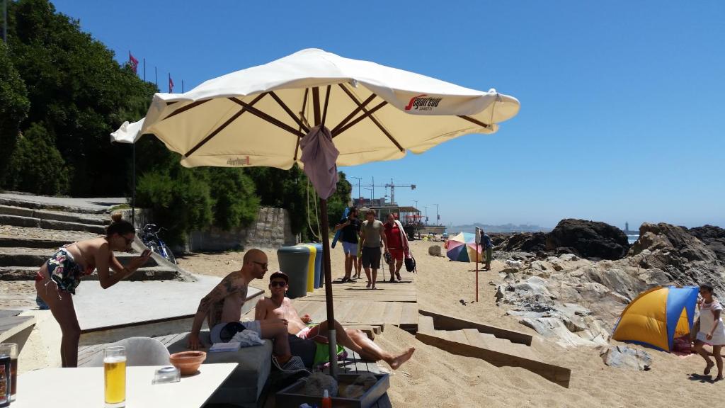 a group of people sitting under an umbrella on the beach at VRS - PORTO BEACH FLAT in Porto