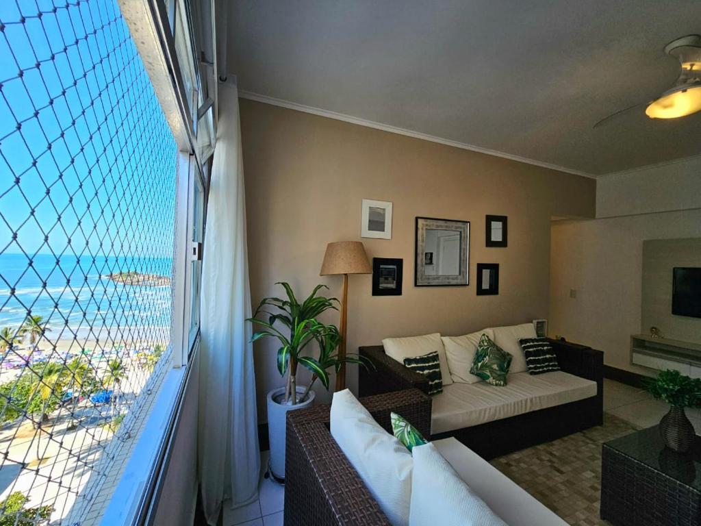 a living room with a couch and a large window at Frente Mar! Apartamento TOP, experiência única! in Guarujá