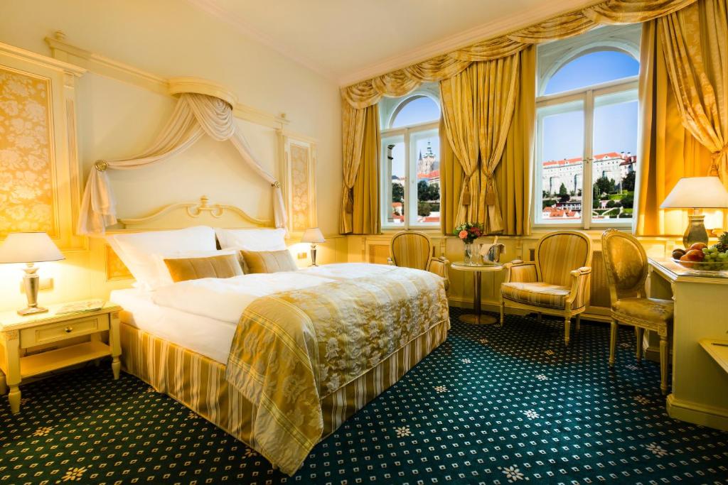 プラハにあるラグジュアリー ファミリー ホテル ロイヤル パレスのベッド、デスク、窓が備わるホテルルームです。