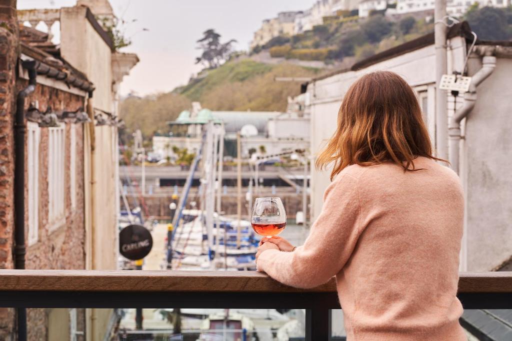a woman standing on a balcony holding a glass of wine at Harbour Breeze - On Torquay's iconic marina with hot tub in Torquay
