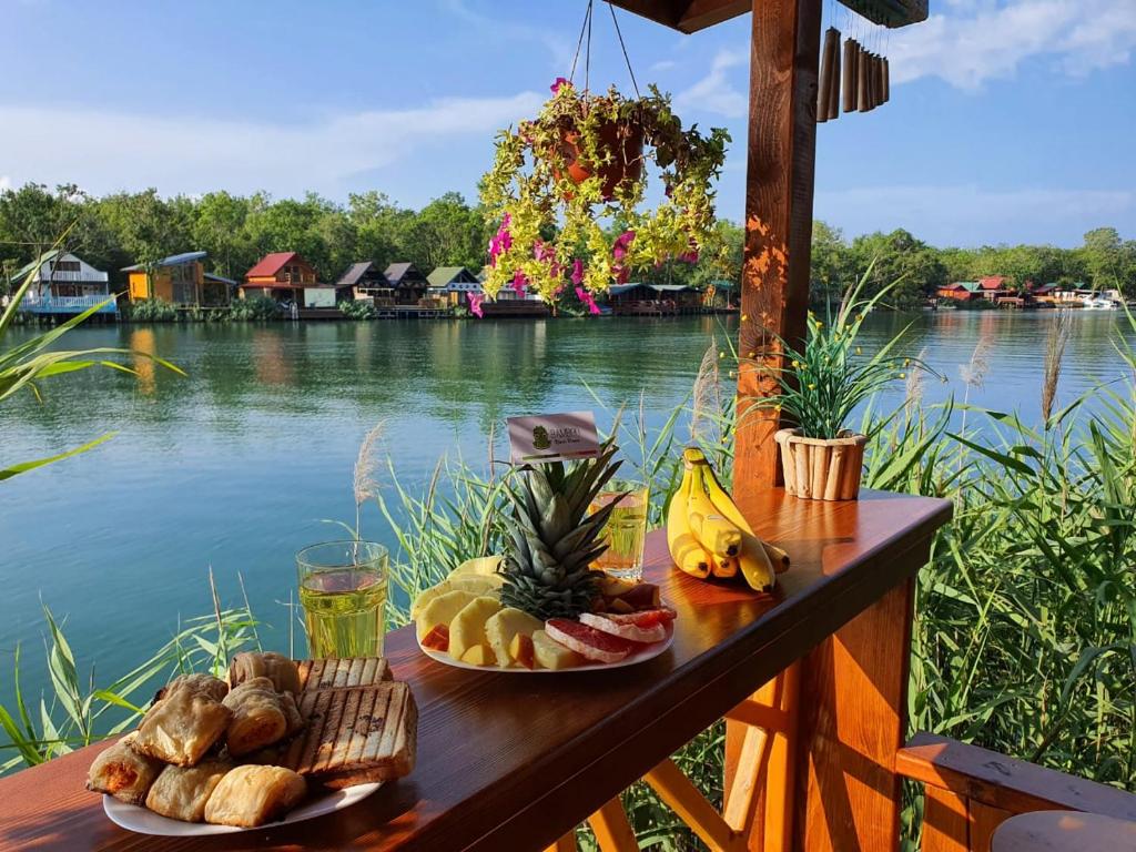 two plates of food on a table next to a body of water at Bamboo River House in Ulcinj