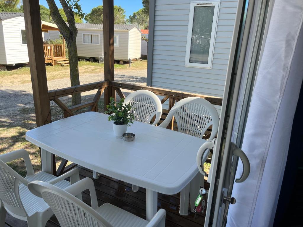 - une table et des chaises blanches sur la terrasse couverte arrière d'une maison dans l'établissement Mobile home camping, au Grau-du-Roi