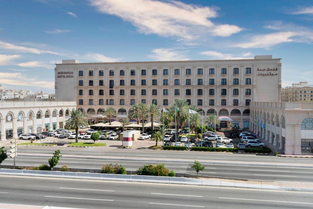 a large building with cars parked in a parking lot at Mövenpick Hotel Jeddah in Jeddah