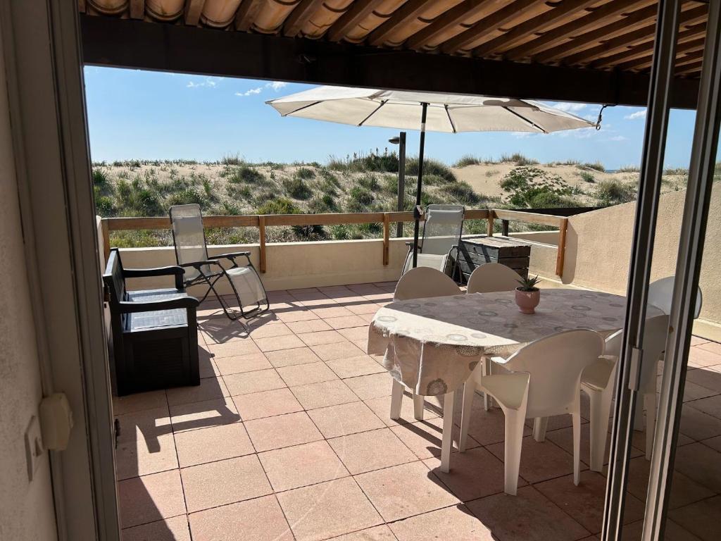 un patio avec une table, des chaises et un parasol dans l'établissement Mooie plek direct aan het strand in Zuid Frankrijk, au Cap d'Agde