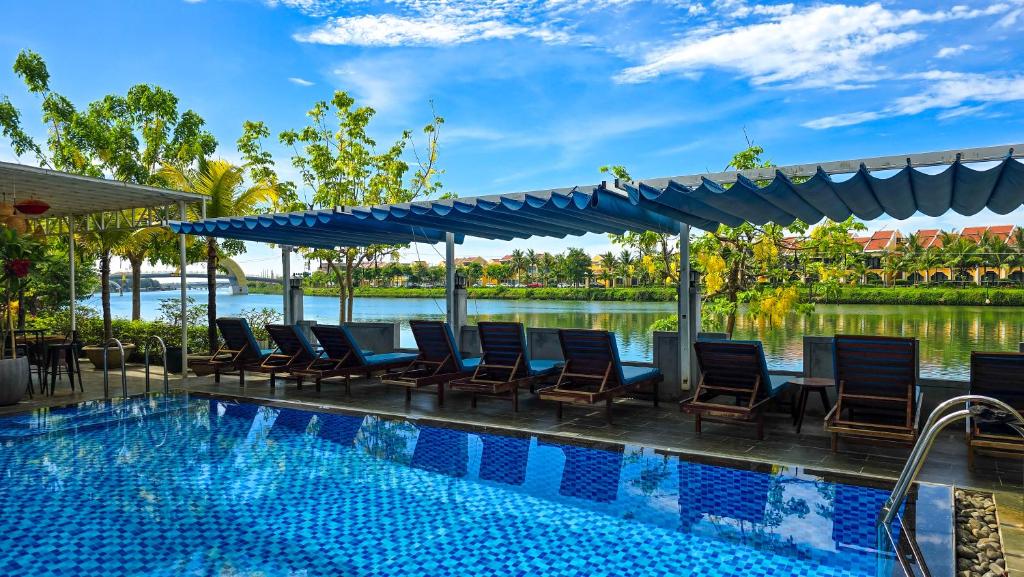 a resort pool with chairs and a view of the water at Riverside White House Hotel in Hoi An