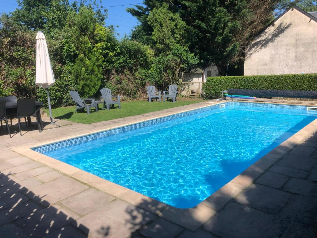 a blue swimming pool with chairs and an umbrella at Daisy Cottage with seasonal Swimming Pool in Le Mesnil-Gilbert