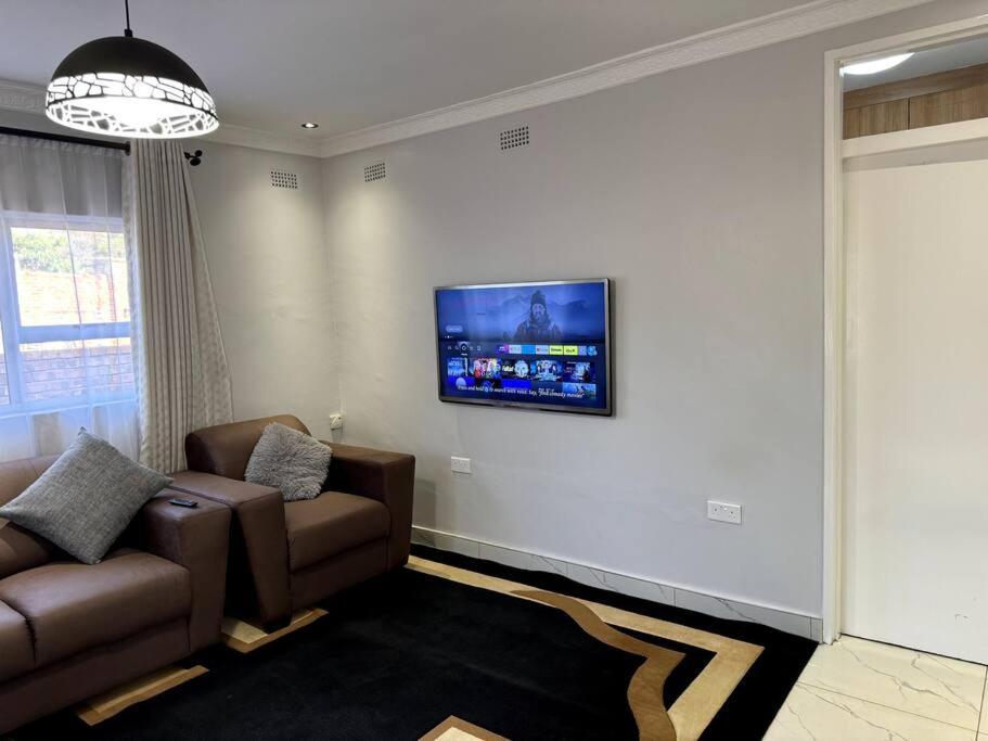a living room with a couch and a tv on the wall at Nid De Chateau in Harare