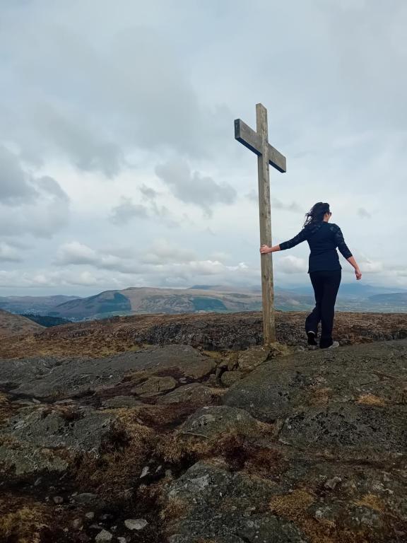 a woman standing next to a wooden cross on a hill at Carlingford Glamping Hut in Rathcor Lower