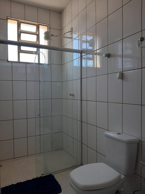 uma casa de banho com azulejos brancos, um WC e uma janela. em Apartamento inteiro e climatizado em Ipatinga