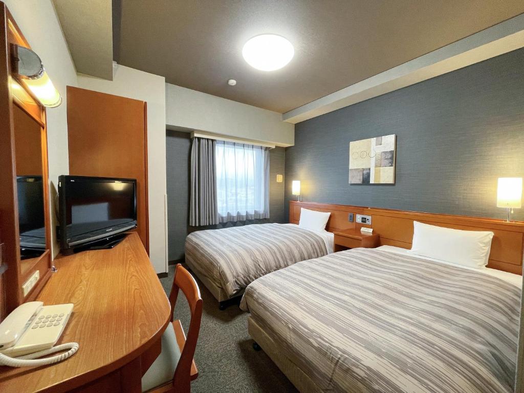 Habitación de hotel con 2 camas, escritorio y TV. en Hotel Route-Inn Fujieda-Eki Kita en Fujieda