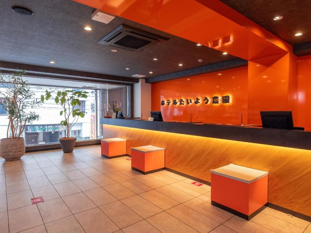 un vestíbulo con paredes de color naranja y un bar con taburetes en Hotel Taiyo Noen Nibancho, en Matsuyama