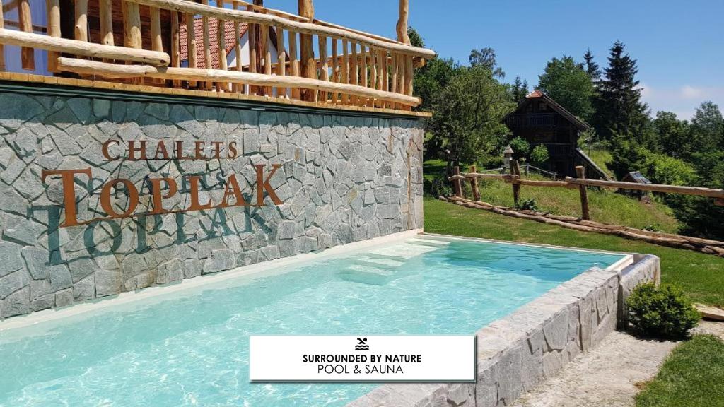 a swimming pool at a resort with a stone wall at Chalets Toplak in Sveti Duh na Ostrem Vrhu