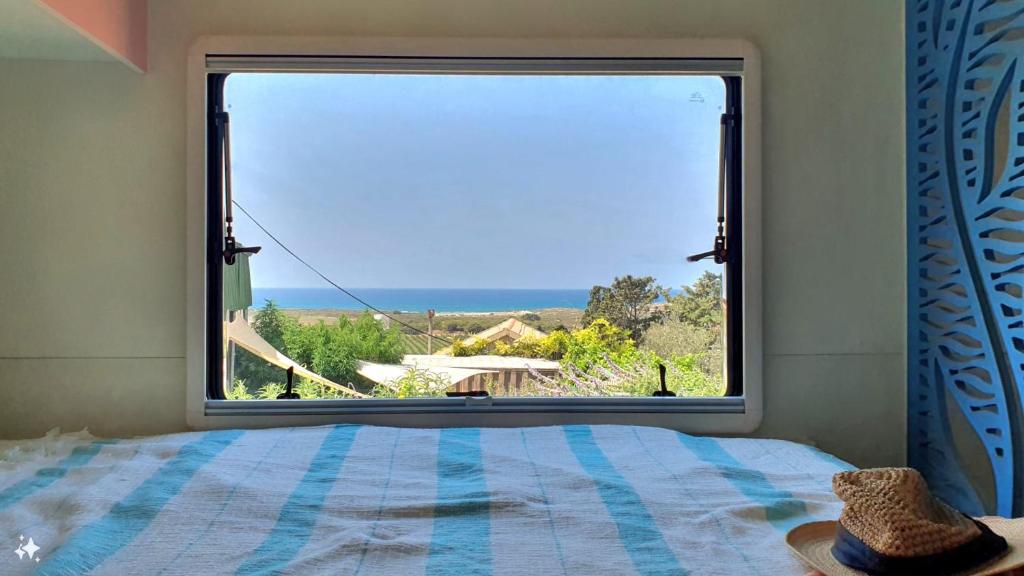a bedroom with a large window with a view of the ocean at Countryside, beach view glamping caravan in HaBonim