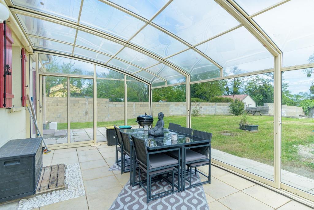 une véranda en verre avec une table et des chaises sur la terrasse dans l'établissement Le Havre Paisible - Belle maison proche de Paris, à Précy-sur-Marne
