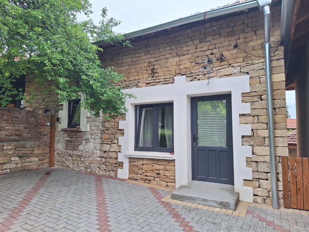 een stenen huis met een zwarte deur en een raam bij Под шарената сянка in Kŭrpachevo
