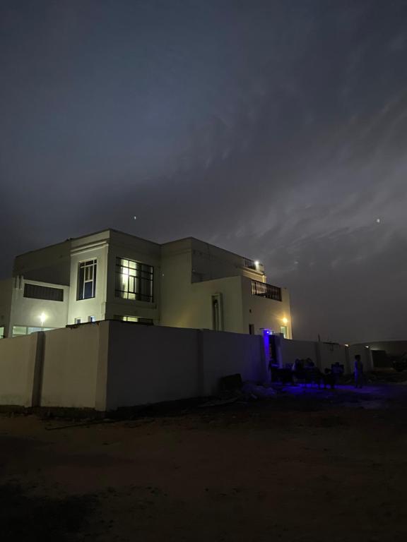 a house lit up at night behind a fence at Al Ashkhara Beach House in Al Ashkharah
