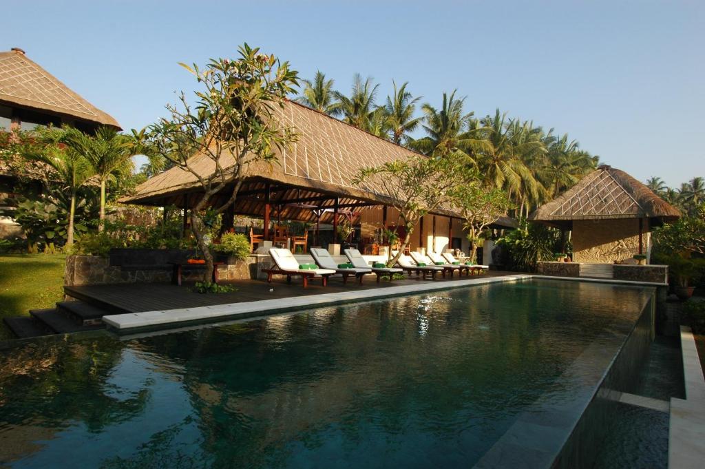 a resort with a swimming pool with chairs and trees at Villa Kanti in Ubud