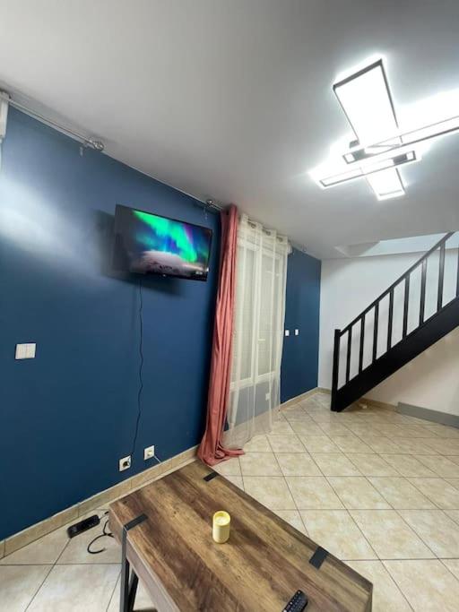 un salon avec une télévision sur un mur bleu dans l'établissement Sweet Harmony - Appart spacieux, à Aulnay-sous-Bois