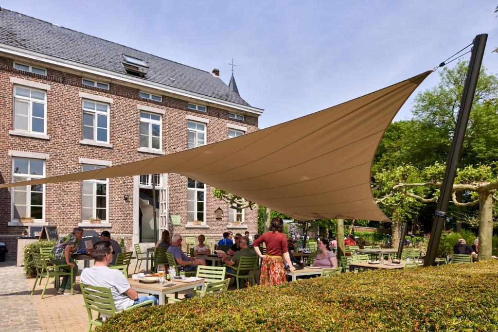 a group of people sitting at tables under a large umbrella at De Pastorie in Borgloon