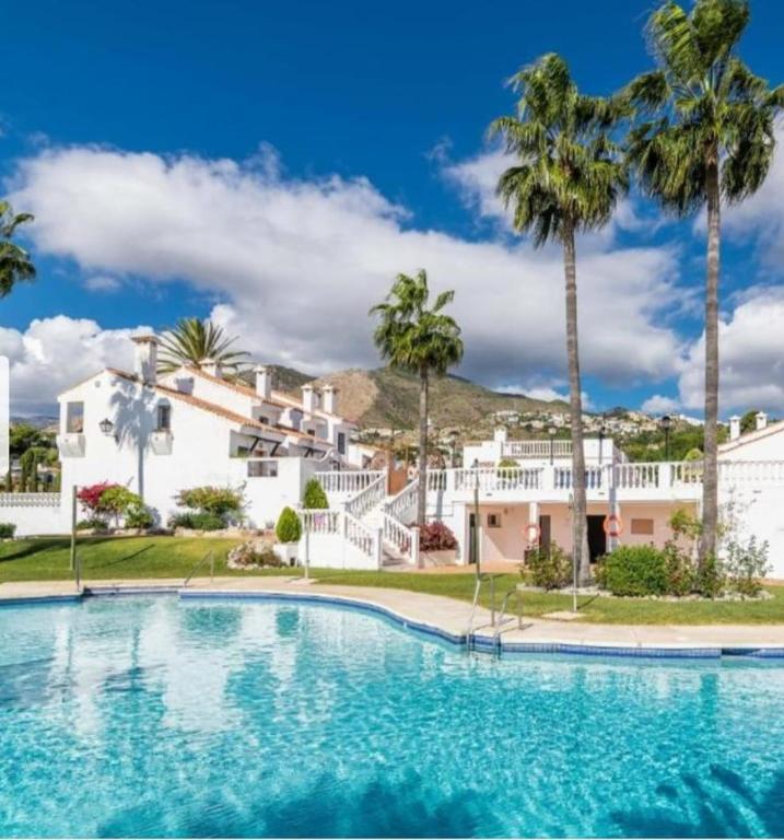 a swimming pool in front of a house with palm trees at casa caravane in Benalmádena