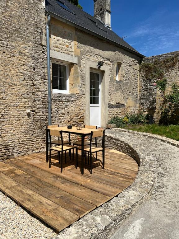 une terrasse en bois avec une table en face d'un bâtiment dans l'établissement Escapade en Baiocensis, à Villiers-le-Sec