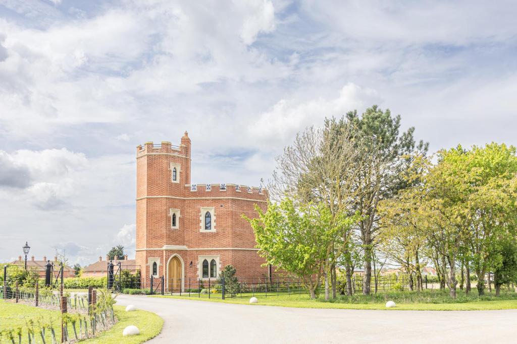 a brick building with a tower on the side of a road at South Lodge, St Osyth Priory in Saint Osyth