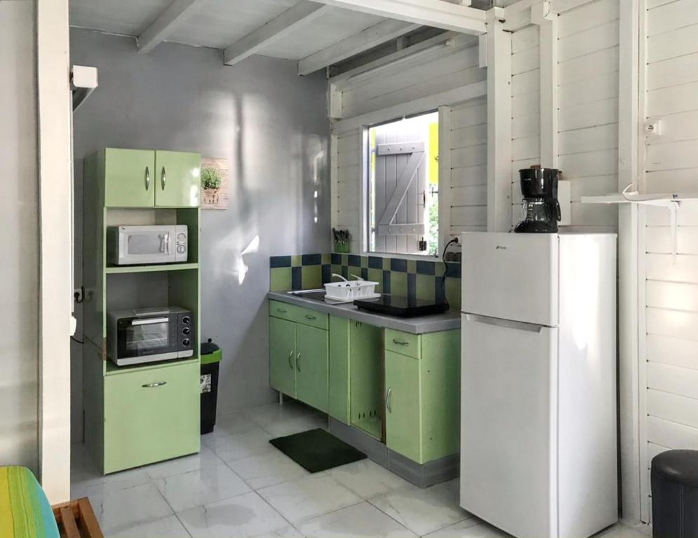 a kitchen with green cabinets and a white refrigerator at Appartement d'une chambre a Le Carbet a 1 m de la plage avec vue sur la mer jardin clos et wifi in Le Carbet
