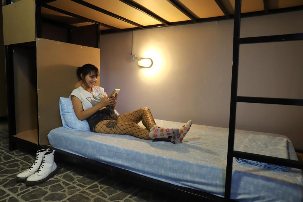 a woman sitting on a bed looking at her cell phone at Asha Hostel in Fortuna