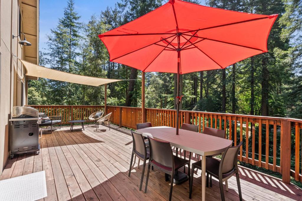 a wooden deck with a table and red umbrellas at Redwood Oasis - Eco-luxury cabin with hot tub in the Santa Cruz Mountains in Ben Lomond