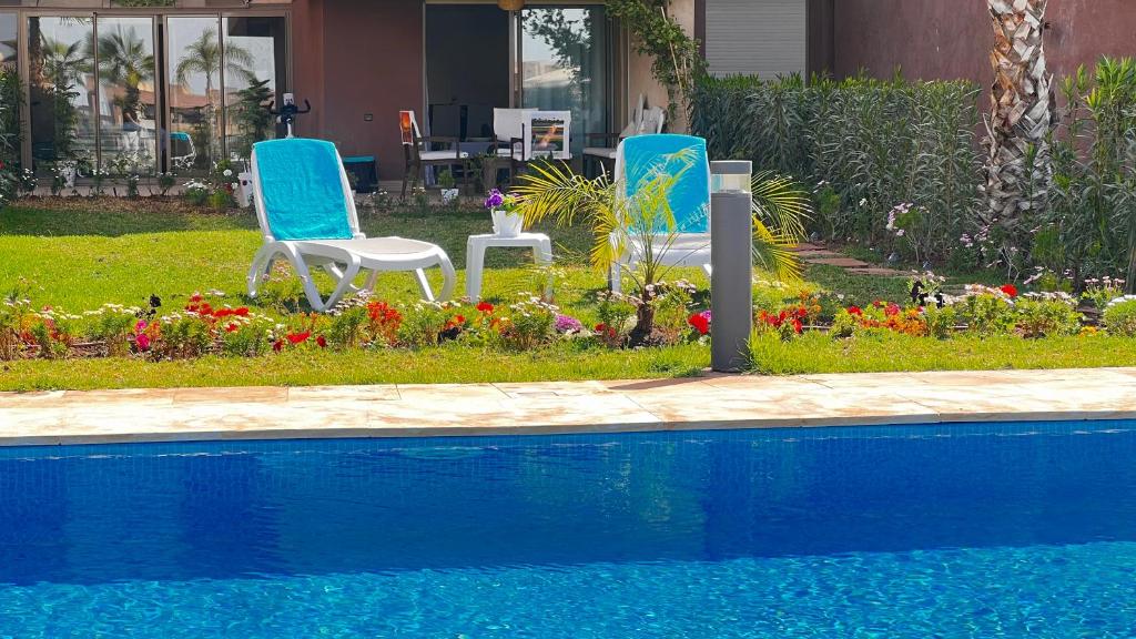two chairs and flowers next to a swimming pool at Prestigia,Golf, piscine, soleil, paysage, sport, spacieux,lux résidence in Marrakesh