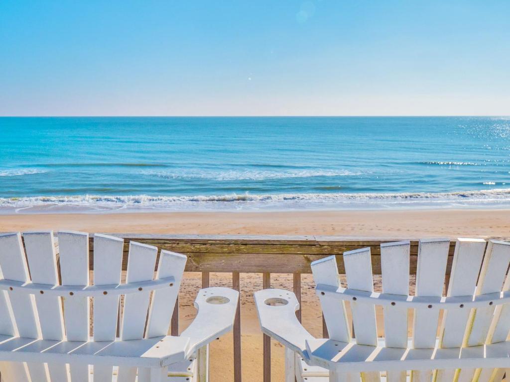 two white chairs sitting on the beach near the ocean at A Grande Green in Surf City