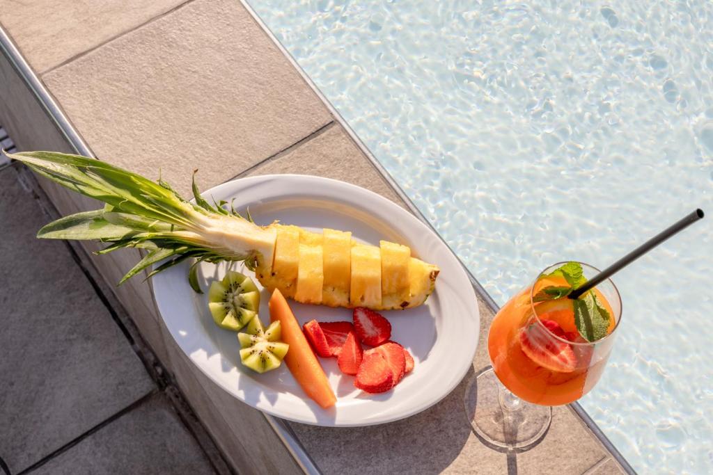 a plate with fruit and a drink next to a pool at Hotel Bristol in Caorle