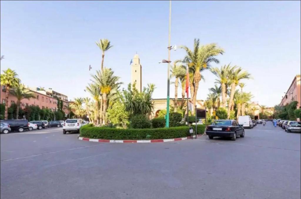 parking z samochodami, palmami i wieżą zegarową w obiekcie Riad les fleurs de Lys de Al qaria Assiyahia w Marakeszu