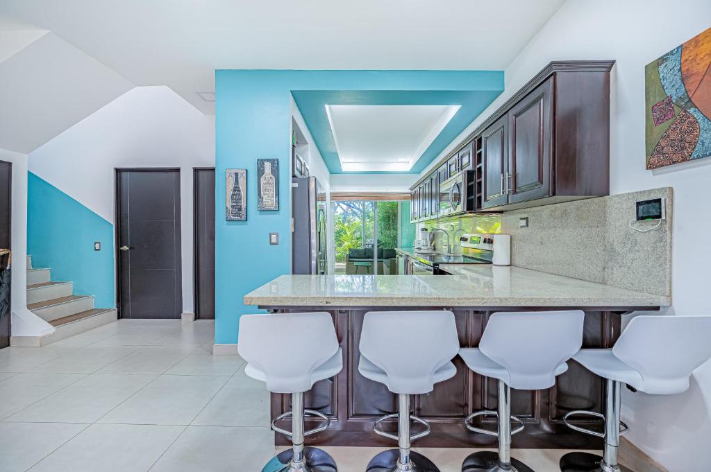 a kitchen with blue walls and a counter with white bar stools at Jacarandas 4 in Tamarindo