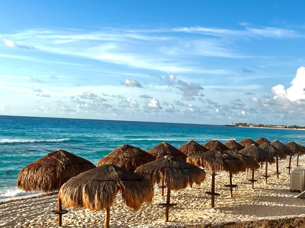 a row of straw umbrellas on a beach with the ocean at Beachfront Resort Studio with Romantic Sunset Views in Cancún