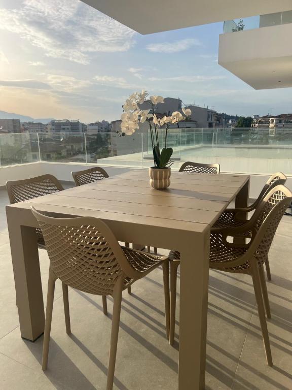 a wooden table with chairs and a vase of flowers on a balcony at White luxury apartment in Tríkala