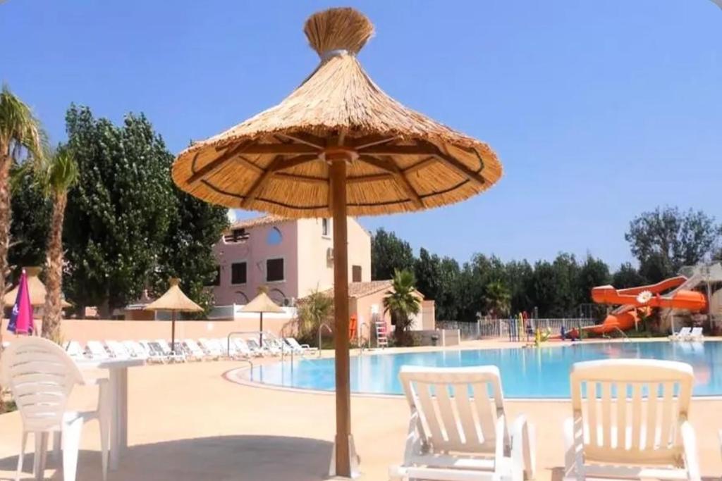 a straw umbrella in front of a swimming pool at **Magnifique Nouveau Bungalow** Village Siblu - Plage - Piscine - Sauna... in Valras-Plage