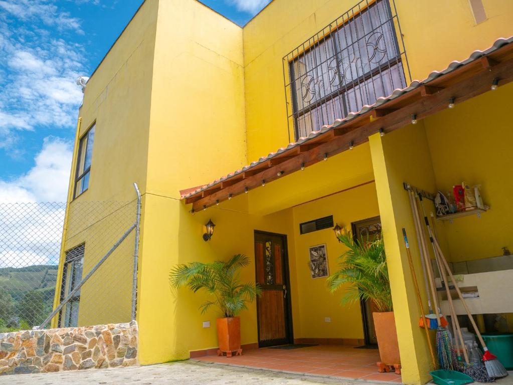 una casa amarilla con palmeras delante en Descanso Bajo La Piedra Del Peñol, en Guatapé