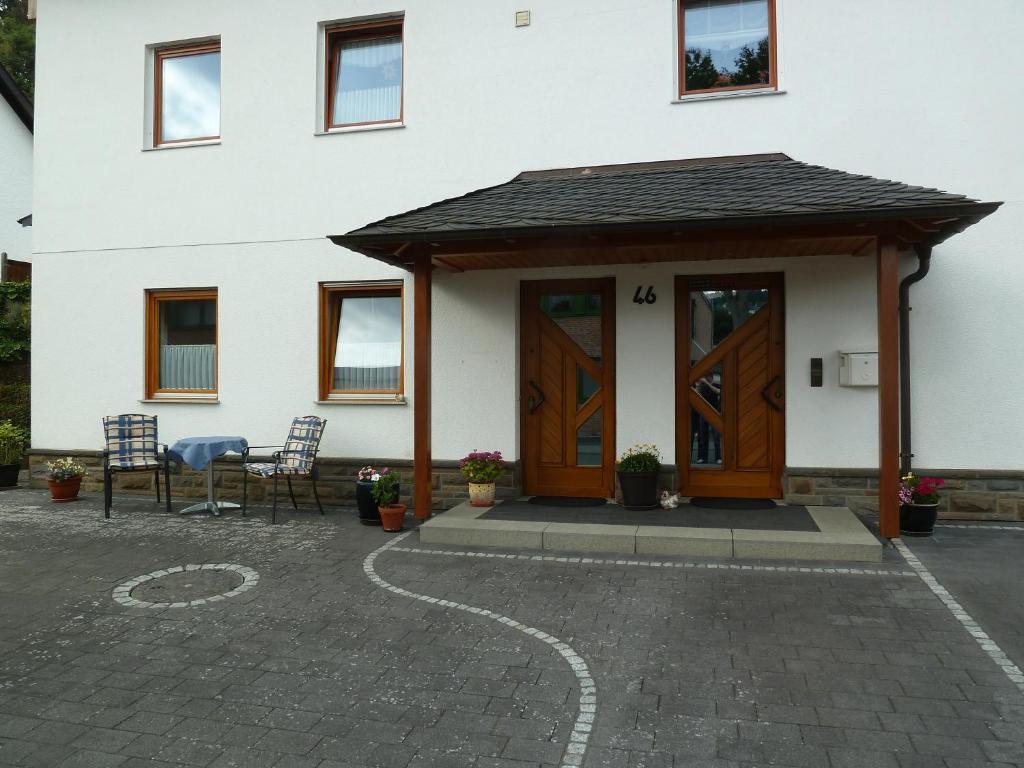 ein weißes Haus mit einer Holztür und Stühlen in der Unterkunft Ferienwohnung Auel in Adenau