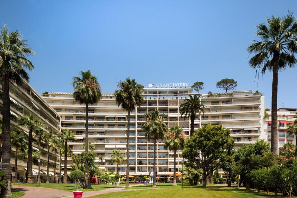 a large building with palm trees in a park at Cannes Luxury Rental - Stunning apartment with terrace to rent Grand Hotel in Cannes
